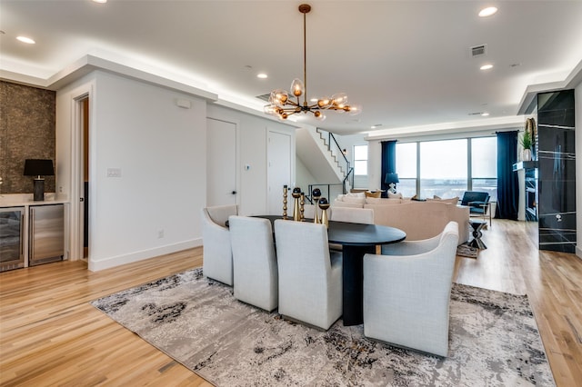 dining room with light hardwood / wood-style floors, beverage cooler, and an inviting chandelier