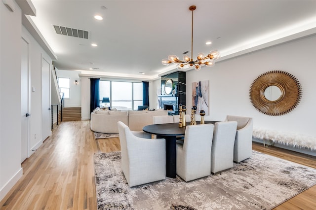 dining area with a fireplace, light hardwood / wood-style floors, and a chandelier