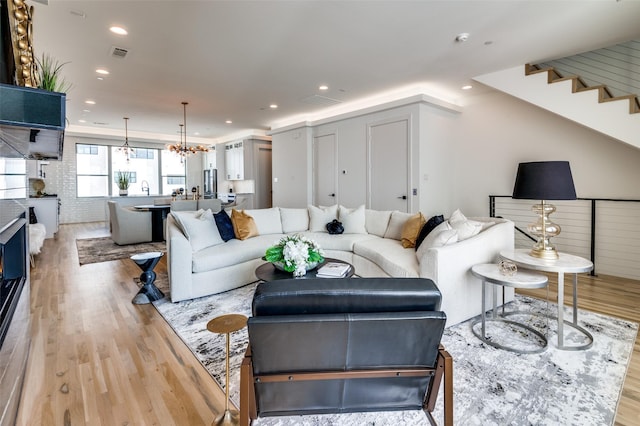 living room featuring sink, light hardwood / wood-style floors, an inviting chandelier, and brick wall