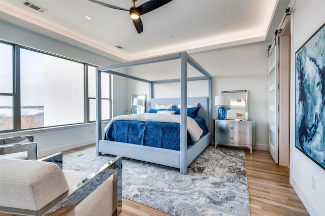 bedroom with hardwood / wood-style floors, ceiling fan, and a barn door