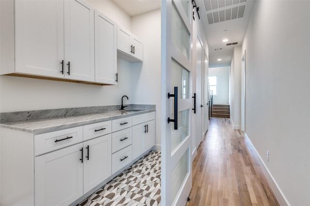 kitchen with white cabinetry, sink, light stone counters, and light wood-type flooring