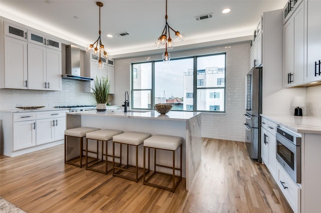 kitchen featuring white cabinets, decorative light fixtures, light hardwood / wood-style flooring, and wall chimney exhaust hood