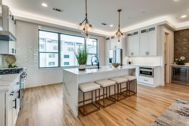 kitchen with sink, premium appliances, light hardwood / wood-style flooring, a kitchen island with sink, and white cabinets