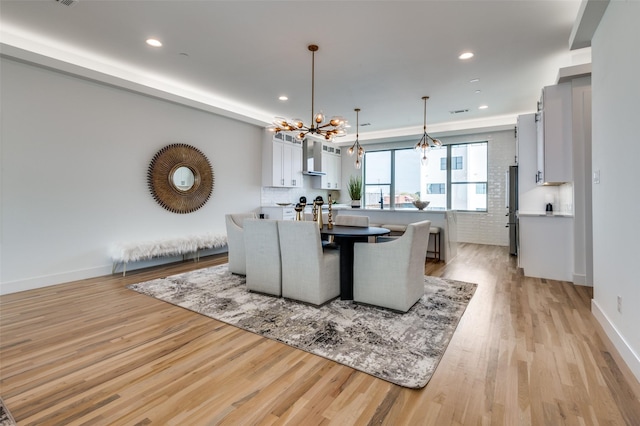 dining area with a notable chandelier, light wood-type flooring, and brick wall