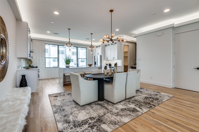 dining space with light wood-type flooring, sink, brick wall, and a chandelier