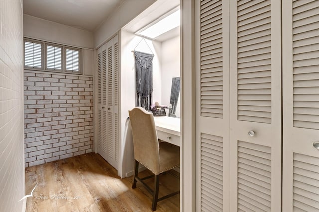 home office with brick wall and light hardwood / wood-style flooring