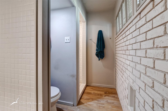 bathroom with hardwood / wood-style floors, brick wall, and toilet