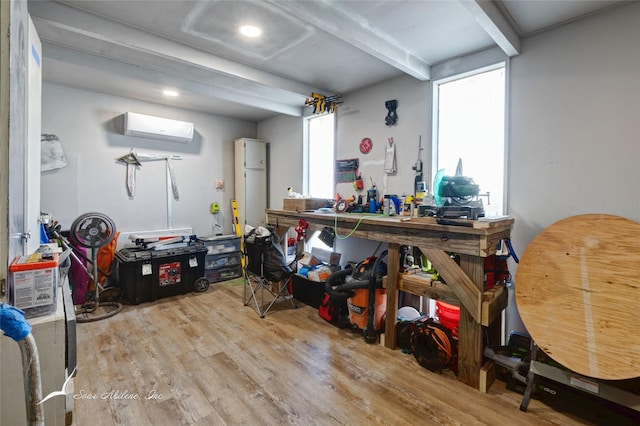 misc room featuring a wall mounted air conditioner, a workshop area, light hardwood / wood-style flooring, and beamed ceiling