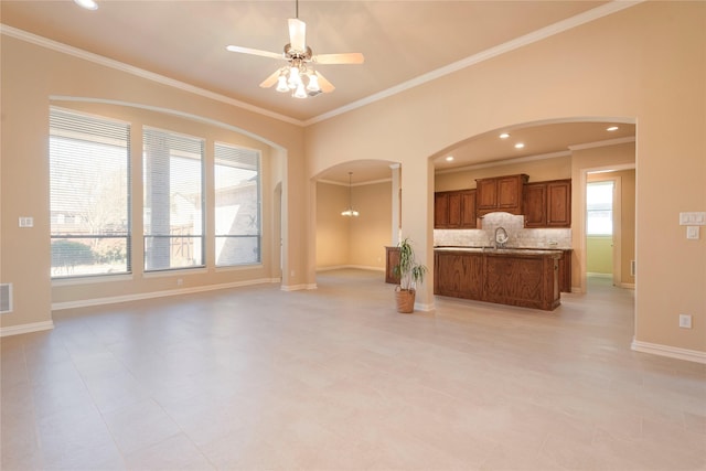 unfurnished living room with arched walkways, a ceiling fan, ornamental molding, a sink, and baseboards