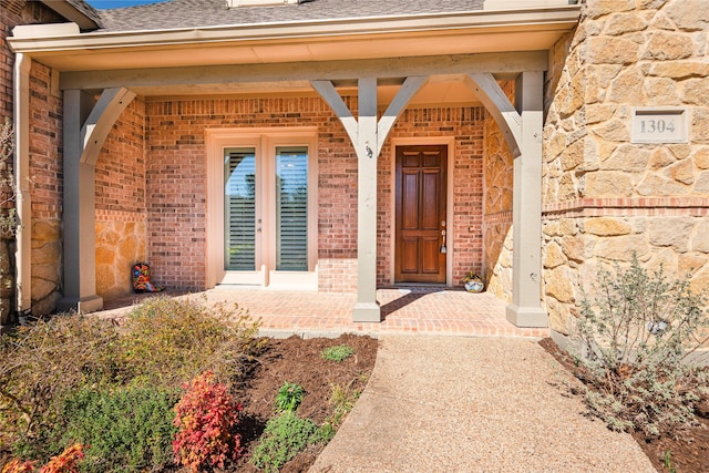 entrance to property featuring stone siding, a shingled roof, and brick siding