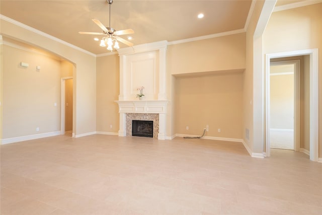 unfurnished living room featuring arched walkways, crown molding, a fireplace, ceiling fan, and baseboards