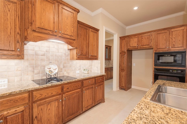 kitchen featuring brown cabinets, light stone countertops, crown molding, black appliances, and a sink