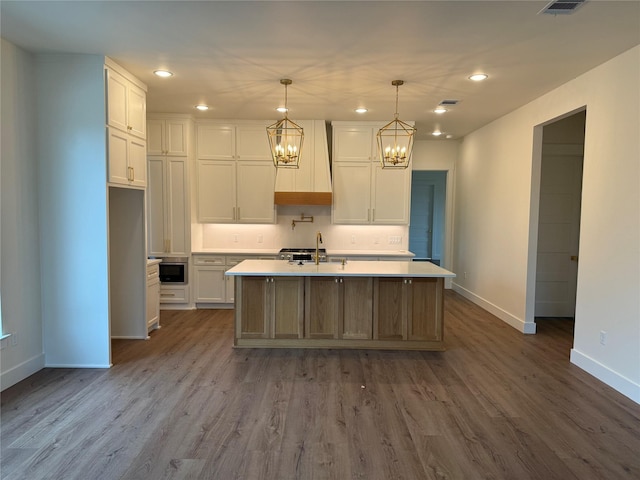 kitchen featuring pendant lighting, a kitchen island with sink, sink, hardwood / wood-style flooring, and white cabinetry