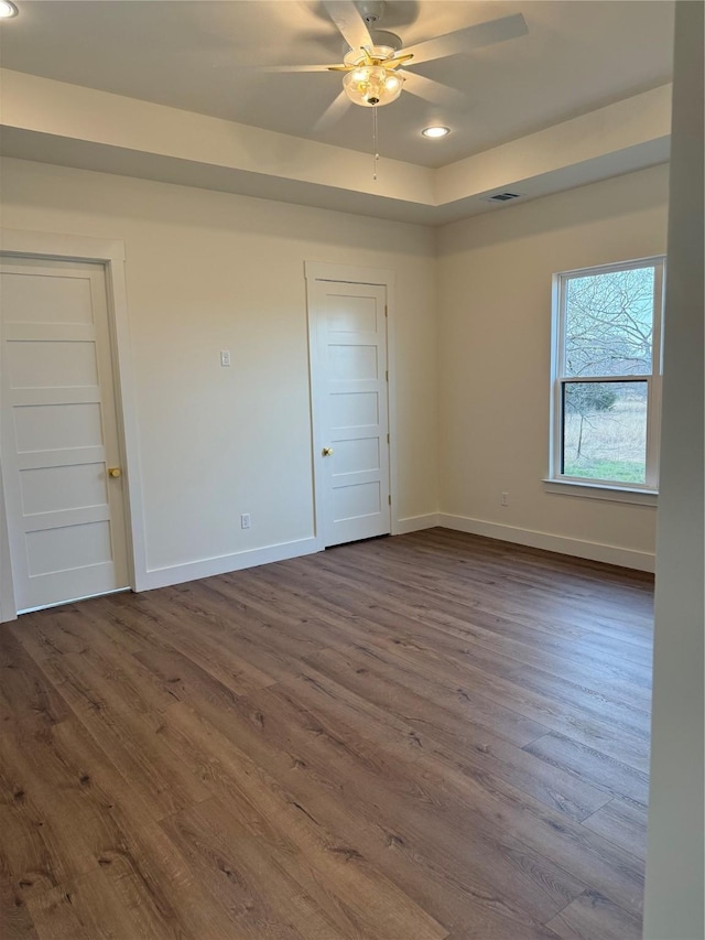 unfurnished room featuring dark wood-type flooring, baseboards, recessed lighting, a raised ceiling, and a ceiling fan