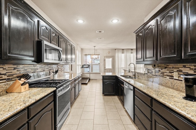 kitchen with decorative light fixtures, sink, light tile patterned floors, light stone counters, and stainless steel appliances