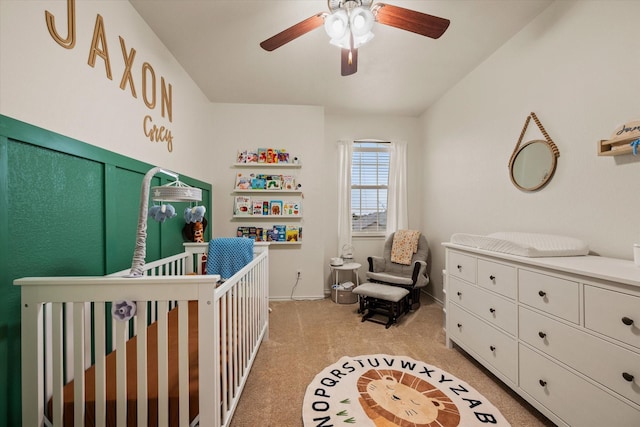 bedroom with a nursery area, light colored carpet, and ceiling fan