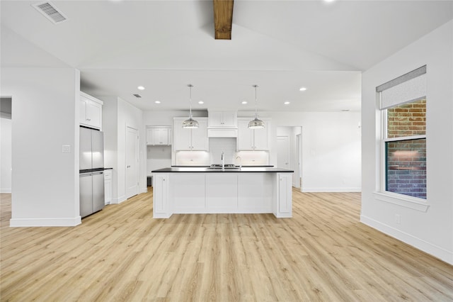 kitchen with a center island with sink, vaulted ceiling with beams, decorative light fixtures, white cabinetry, and stainless steel refrigerator