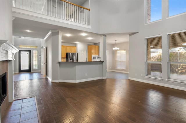 unfurnished living room featuring dark wood-type flooring, a healthy amount of sunlight, a high ceiling, and a notable chandelier