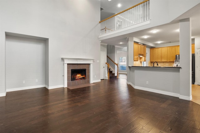 unfurnished living room featuring sink, a towering ceiling, a fireplace, and dark hardwood / wood-style floors