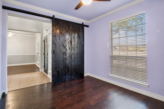 empty room featuring hardwood / wood-style flooring, crown molding, a barn door, and ceiling fan