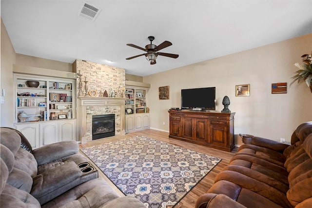 living area with light wood-style floors, ceiling fan, visible vents, and a stone fireplace