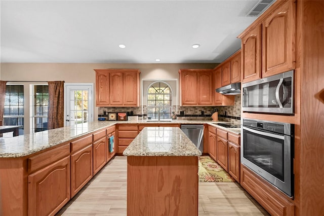 kitchen featuring light stone counters, stainless steel appliances, a kitchen island, a sink, and under cabinet range hood