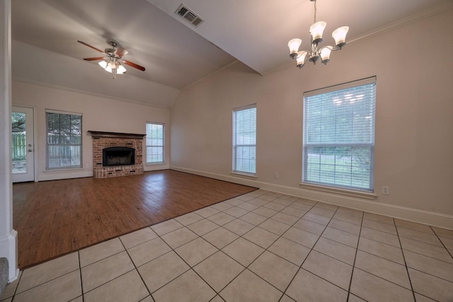 unfurnished living room featuring crown molding, a fireplace, light tile patterned flooring, ceiling fan with notable chandelier, and vaulted ceiling