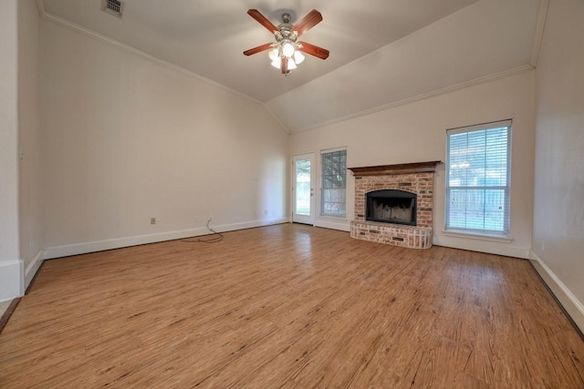 unfurnished living room featuring vaulted ceiling, light hardwood / wood-style floors, a brick fireplace, and a wealth of natural light