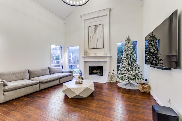 living room with high vaulted ceiling, a fireplace with flush hearth, baseboards, wood-type flooring, and crown molding