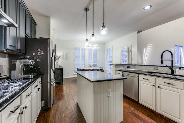 kitchen featuring appliances with stainless steel finishes, dark wood-type flooring, a center island, wall chimney range hood, and a sink