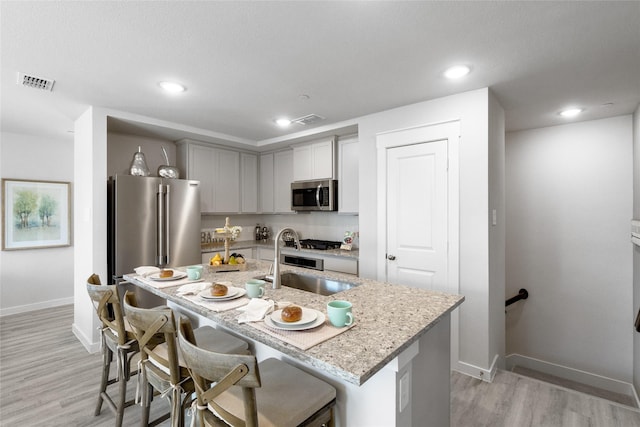 kitchen featuring light wood-type flooring, stainless steel appliances, sink, a center island with sink, and a breakfast bar area