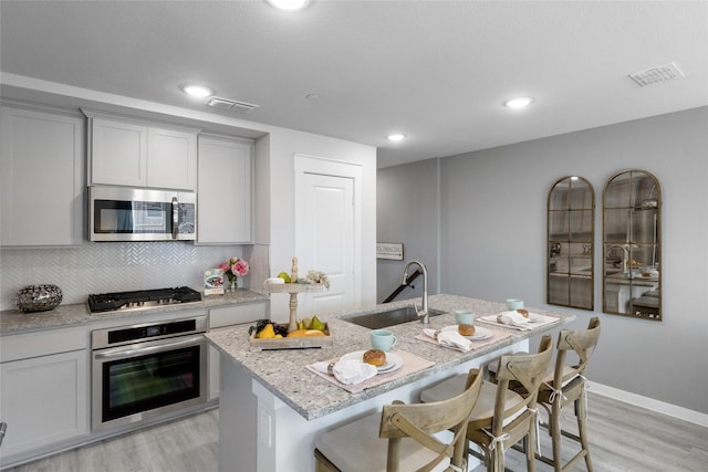 kitchen featuring a center island with sink, sink, light hardwood / wood-style flooring, light stone counters, and stainless steel appliances