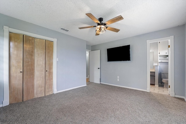 unfurnished bedroom with ceiling fan, ensuite bathroom, a closet, and light carpet