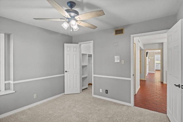 unfurnished bedroom featuring light carpet, a closet, a spacious closet, and ceiling fan