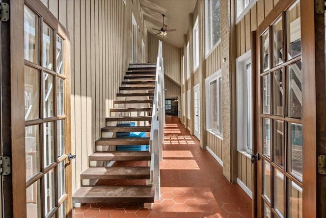 staircase with tile patterned flooring, ceiling fan, wood walls, and a towering ceiling