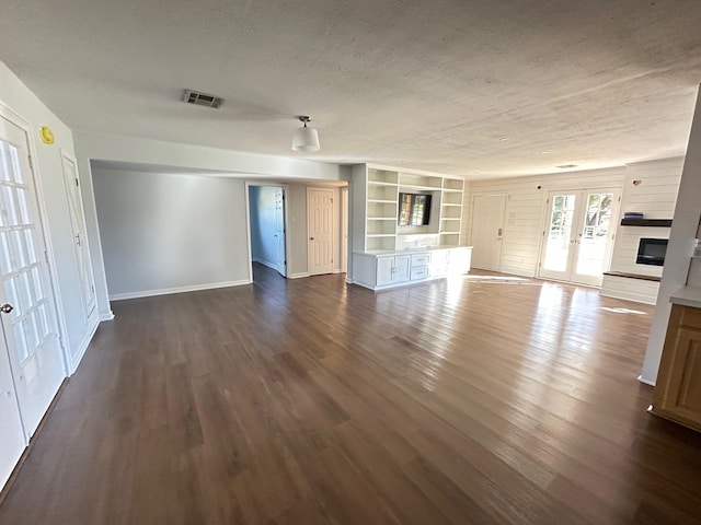 unfurnished living room featuring built in features, french doors, dark hardwood / wood-style floors, and a textured ceiling