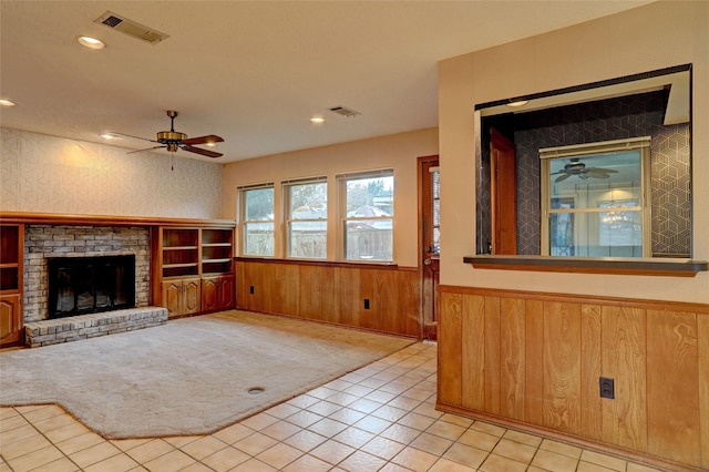 unfurnished living room featuring wooden walls, ceiling fan, a fireplace, and light carpet