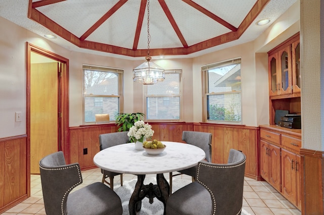 tiled dining area with lofted ceiling, a chandelier, and wooden walls