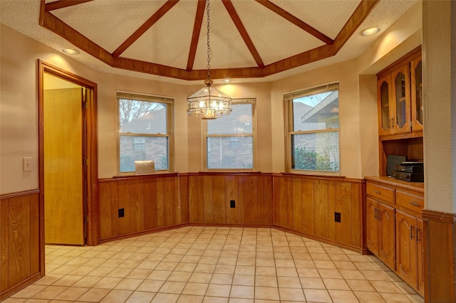 unfurnished dining area with vaulted ceiling, wooden walls, and a chandelier