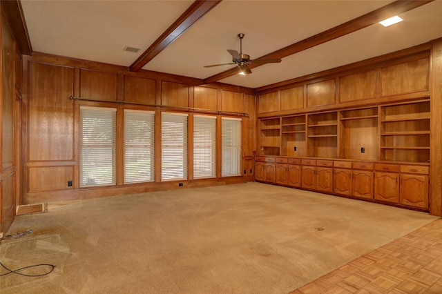 unfurnished living room featuring beam ceiling, wooden walls, light colored carpet, and ceiling fan