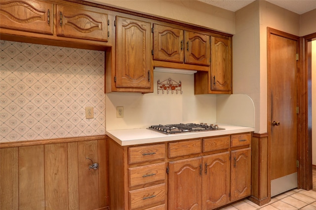 kitchen with stainless steel gas stovetop, light tile patterned floors, and wood walls