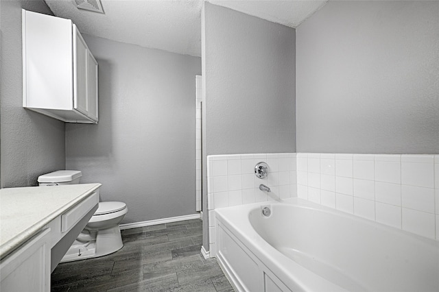 bathroom featuring toilet, a textured ceiling, vanity, a bath, and hardwood / wood-style floors