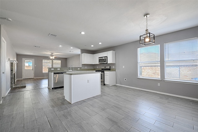 kitchen featuring sink, light wood-type flooring, appliances with stainless steel finishes, pendant lighting, and white cabinets