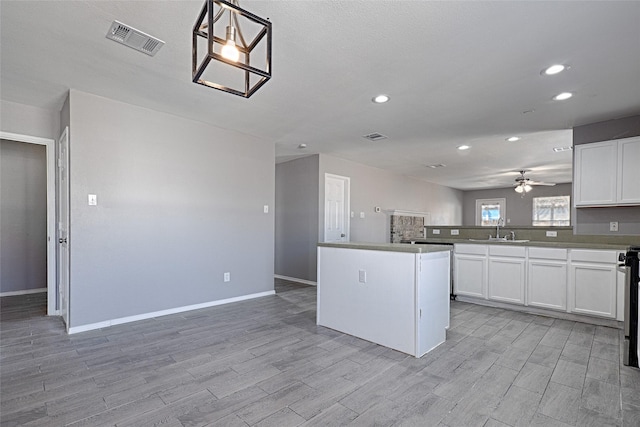 kitchen with hanging light fixtures, sink, white cabinets, and light wood-type flooring