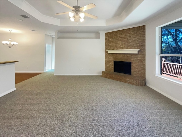 unfurnished living room with ceiling fan with notable chandelier, a raised ceiling, ornamental molding, and a fireplace