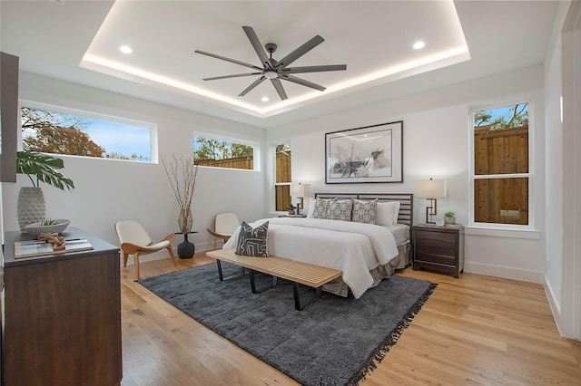 bedroom with light hardwood / wood-style floors, a raised ceiling, and ceiling fan