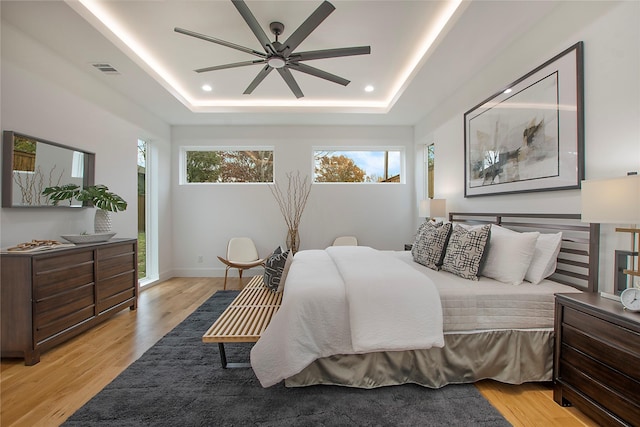 bedroom with ceiling fan, light wood-type flooring, and a tray ceiling