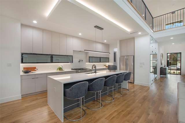 kitchen featuring decorative light fixtures, light hardwood / wood-style flooring, a kitchen island with sink, and high end refrigerator