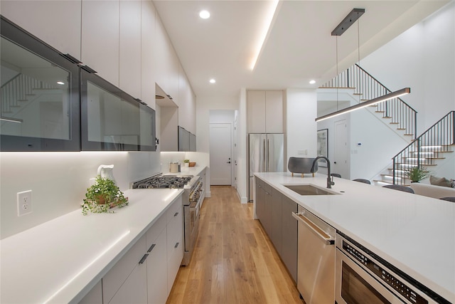 kitchen featuring light wood-type flooring, premium appliances, sink, white cabinets, and hanging light fixtures