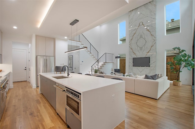 kitchen with appliances with stainless steel finishes, light wood-type flooring, a kitchen island with sink, sink, and decorative light fixtures